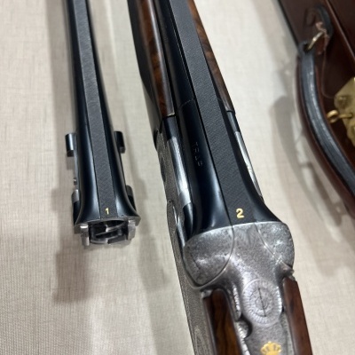 Duas espingardas de canos paralelos com coronhas de madeira castanha e canos pretos, uma com número 2 em amarelo e símbolo de coroa.