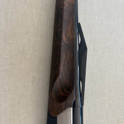 Arma Benelli Armi com madeira trabalhada e parte metálica gravada sobre fundo bege claro