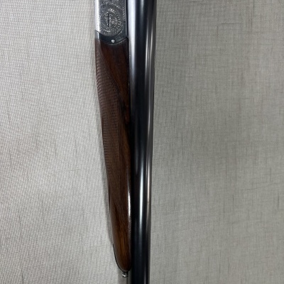 Espingarda com canos duplos em metal preto e madeira escura sobre tecido cinzento