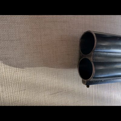 Ponta de arma de canos duplos em metal preto sobre tecido bege com textura