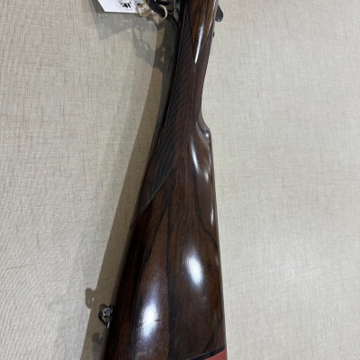 Espingarda com coronha de madeira escura e acabamento texturizado em superfície bege