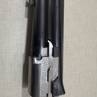 Parte frontal de arma de fogo em metal preto e cinzento sobre fundo bege.