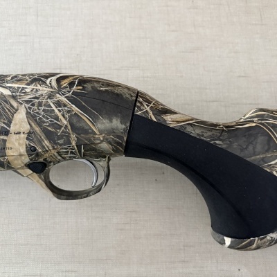 Parte de espingarda camuflada com padrão vegetação seca e punho preto em fundo bege