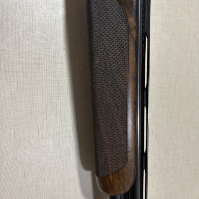 Espingarda com coronha em madeira castanha e canos metálicos pretos com aviso em inglês