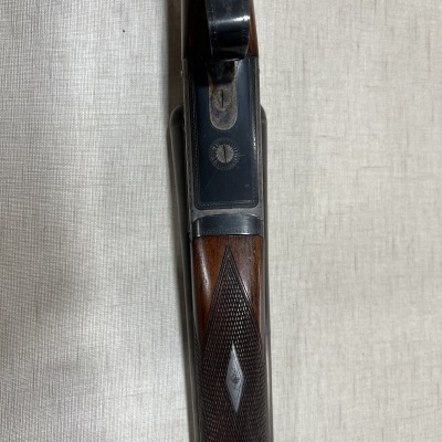 Espingarda com coronha de madeira e metal prateado, aberta, sobre fundo claro