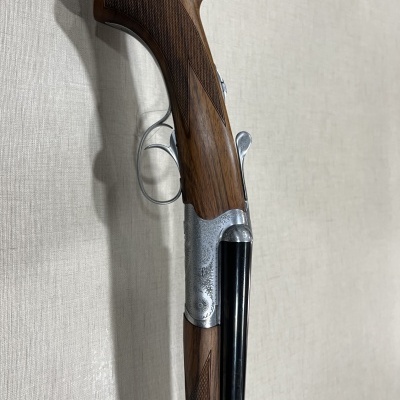 Espingarda de canos duplos em madeira castanha e metal prateado contra parede clara