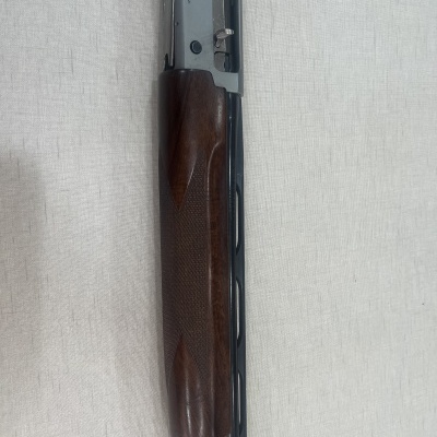 Espingarda com cano preto e coronha em madeira polida sobre tecido claro