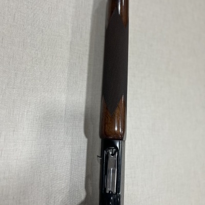 Espingarda com coronha em madeira e partes metálicas pretas sobre superfície clara