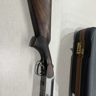 Espingarda em madeira e metal ao lado de mala preta com detalhes dourados