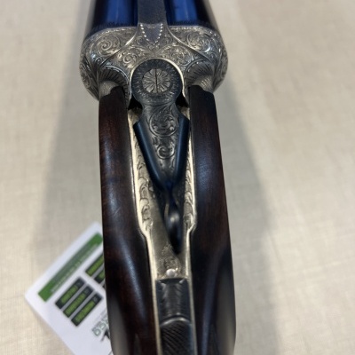 Espingarda de canos duplos com detalhes gravados em metal prateado e madeira escura.