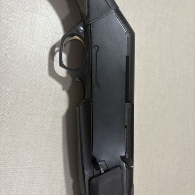 Parte de arma de fogo preta com gatilho dourado em superfície bege.