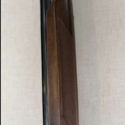 Parte de arma com madeira castanha e metal preto sobre fundo claro