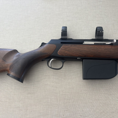 Rifle com coronha em madeira castanha e arma metálica preta sobre fundo bege texturizado.