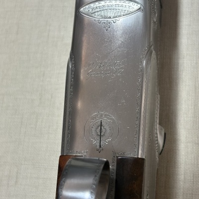 Parte superior metálica de arma de fogo com gravações decorativas e alça em madeira castanha escura