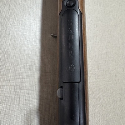 Detalhe da parte superior de uma espingarda com metal preto e gravação SAUER