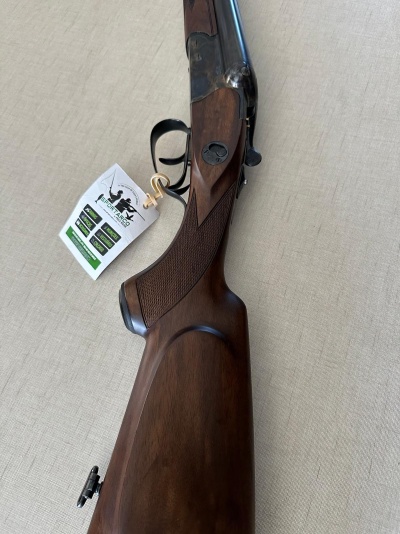 Espingarda com coronha em madeira castanha escura e detalhes em aço escuro sobre superfície bege.
