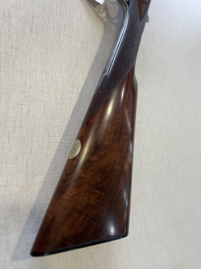 Coronha de espingarda em madeira castanha com punho texturizado escuro e medalha metálica embutida