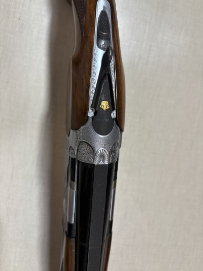 Parte superior de espingarda com decoração engravada e coronha de madeira castanha.