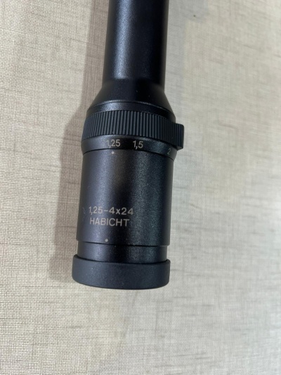 Luneta preta metálica com inscrições e anel de ajuste sobre superfície clara