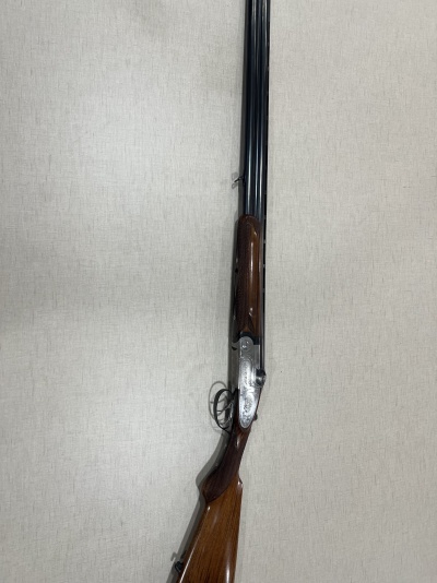 Espingarda de canos duplos em metal preto e madeira castanha com acabamento gravado