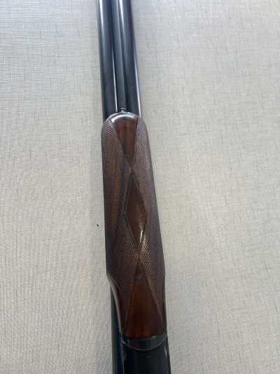 Arma de fogo com canos pretos e empunhadura de madeira escura em tecido cinzento