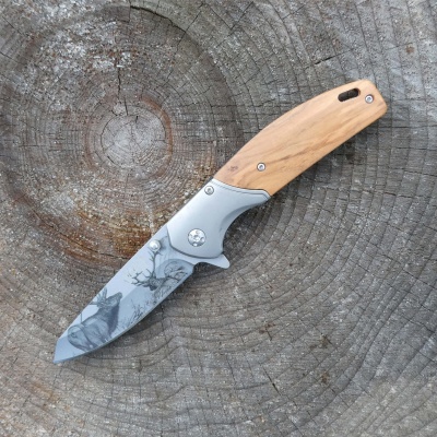 Faca de bolso com lâmina decorada e cabo de madeira sobre tronco cortado