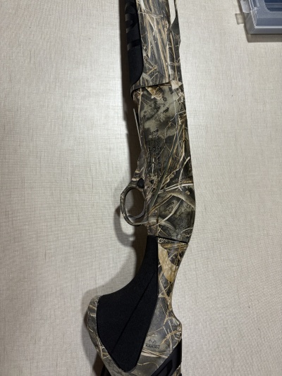 Arma de caça camuflada com padrão Realtree MAX-7, foco na parte traseira e gatilho.