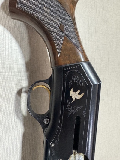 Parte de arma de fogo com cabo madeira castanha e corpo metálico preto com gravura dourada