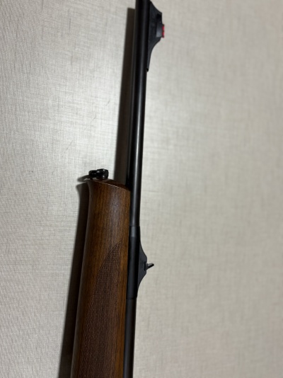 Espingarda com coronha em madeira escura encostada numa parede cinzenta.