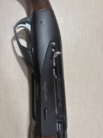 Espingarda Raffaello com coronha de madeira e corpo preto com gravações visíveis.