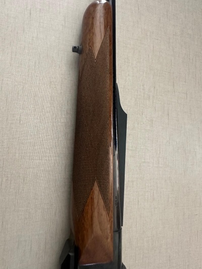 Parte lateral de arma com cabo de madeira castanha texturizada junto a parede bege