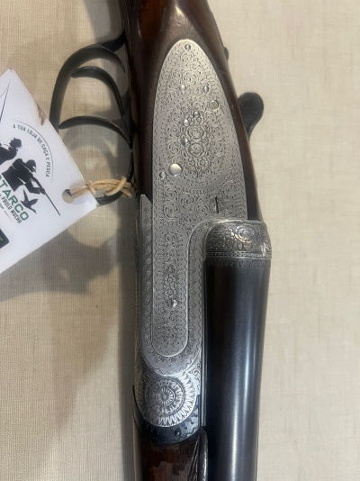 Espingarda com detalhes em metal gravado e madeira escura sobre tecido bege