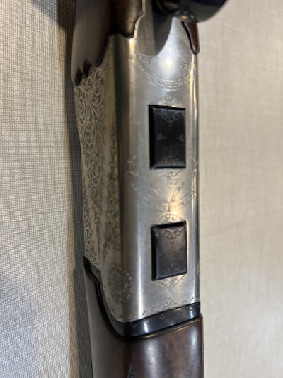 Espingarda com detalhes em metal gravado e madeira escura sobre fundo de tecido claro