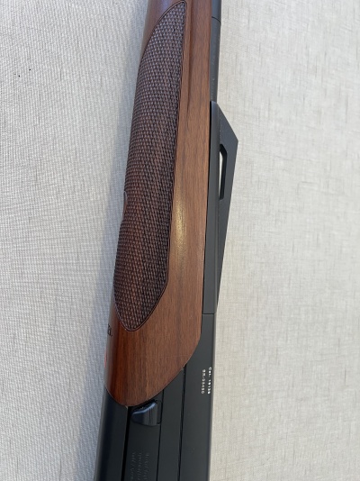 Espingarda com coronha de madeira castanha e corpo metálico preto sobre tecido claro.