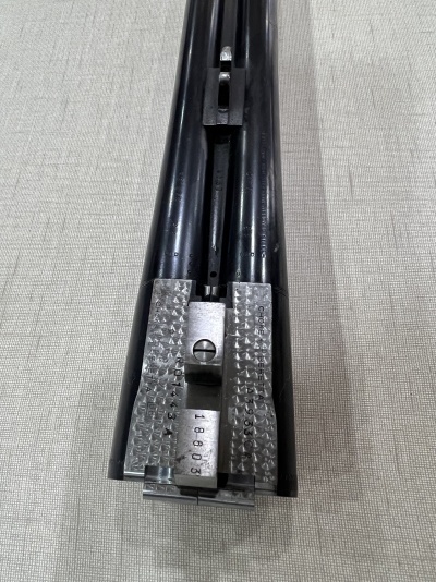 Parte frontal de arma de canos duplos em metal preto com peças metálicas prateadas na base