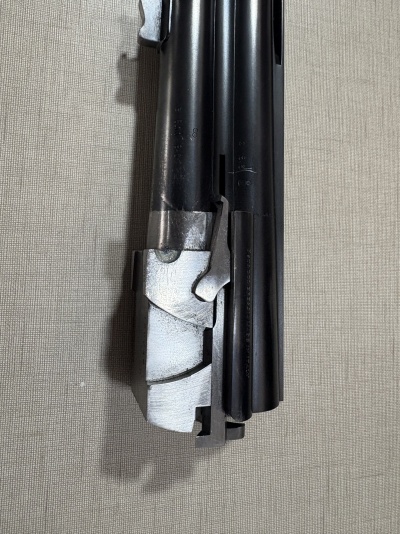 Parte frontal de uma arma de fogo metálica em preto e prateado sobre tecido cinzento.