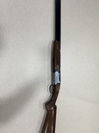 Espingarda de canos duplos com madeira castanha e canos pretos encostada a parede clara