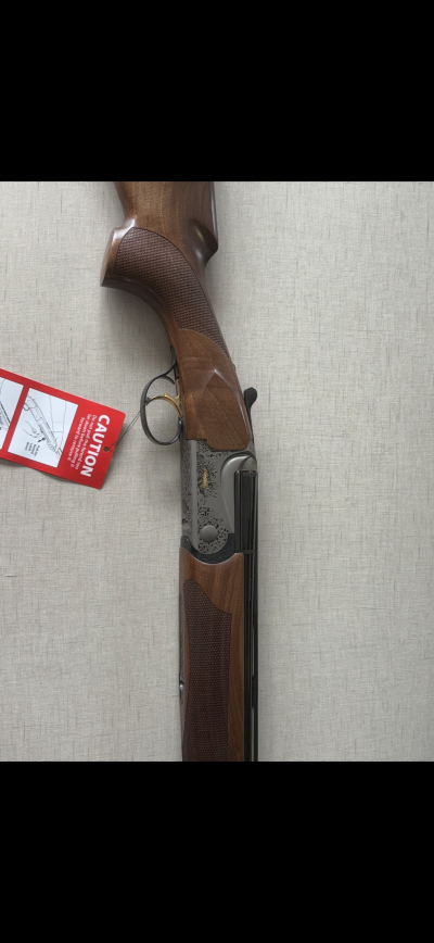 Espingarda com madeiras e detalhes metálicos decorativos, etiqueta vermelha CAUTION, fundo cinza claro.