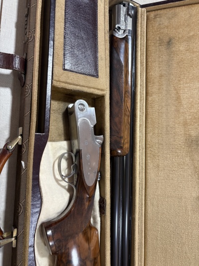 Espingarda desmontada em estojo de tecido bege e couro castanho.