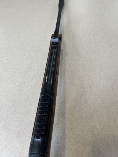 Espingarda com empunhadura preta e corpo em madeira escura sobre tecido bege