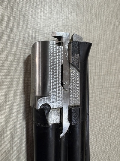 Parte superior de arma de fogo metálica com detalhes gravados em negro e metal polido