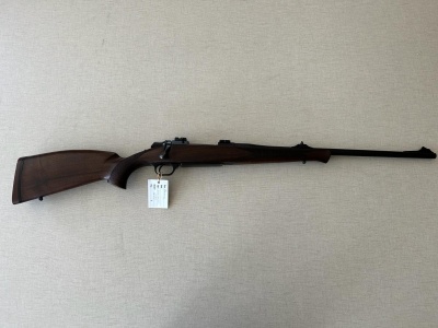 Rifle de madeira escura com cano metálico longo e luneta em superfície bege