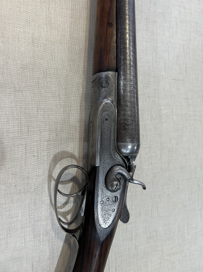 Espingarda de dois canos com madeira escura e detalhes em metal grabado