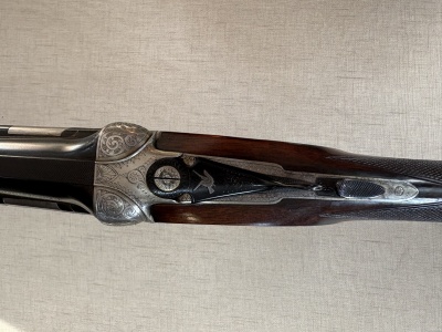 Espingarda de caça com madeira e metal gravado em fundo bege