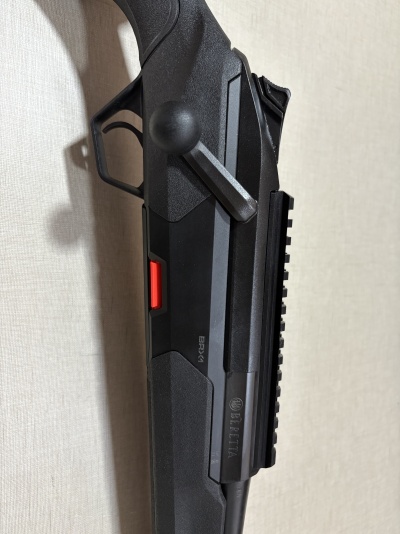 Rifle preto BERETTA BRX-4 com detalhe vermelho encostado numa parede clara