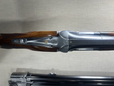 Arma de caça com coronha em madeira e corpo metálico sobre fundo claro