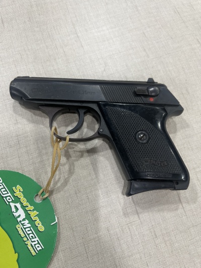 Pistola preta Walther com pega preta texturizada em superfície clara com etiqueta verde ao lado.