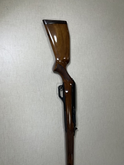 Carabina de madeira polida com detalhes em metal preto encostada numa parede clara