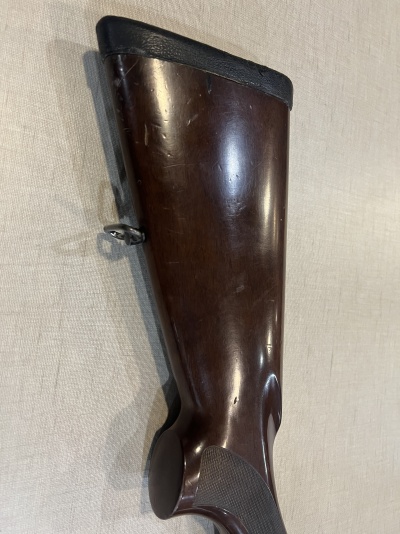 Parte traseira de coronha de arma de fogo em madeira castanho escuro com parte superior preta.