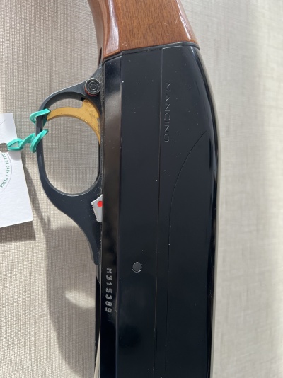 Arma de fogo com cabo em madeira e corpo metálico preto com inscrições NANCION e M315399